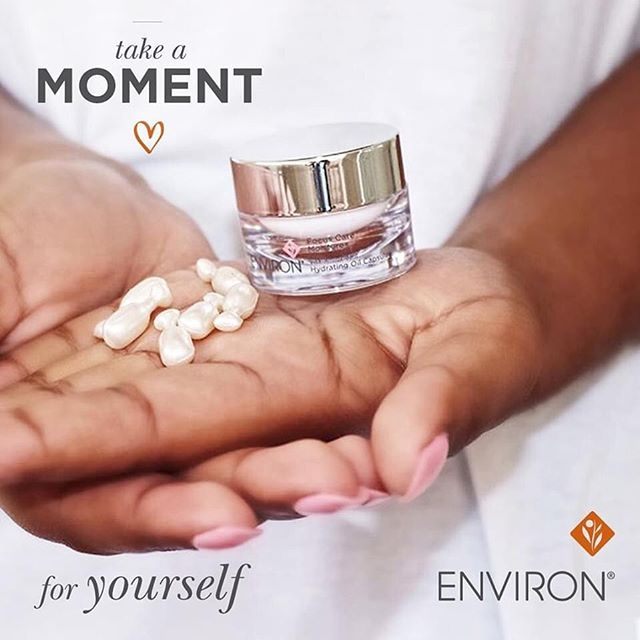 Eine Hand mit hellrosa lackierten Nägeln hält eine transparente Dose Environ Hydrating Oil Capsules. In der Handfläche liegen mehrere weiße, ovale Öl-Kapseln mit Vitaminen und Antioxidantien für geschmeidige Haut und Feuchtigkeit.