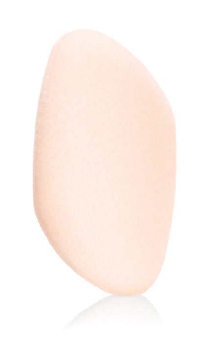 Esponja de maquillaje melocotón claro, suave y aterciopelada, de forma redondeada irregular sobre fondo blanco reflectante. La esponja Flocked Sponge de Jane Iredale tiene textura ligeramente rugosa, ideal para maquillaje líquido o en polvo.