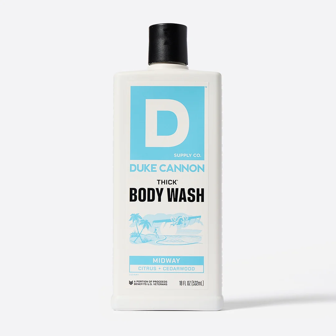 White, rectangular DUKE CANNON THICK Body Wash bottle with a black screw cap. Light blue and white label featuring a large ‘D’ logo, brand name, product name and an illustration of an island. Fragrance: Midway Citrus + Cedarwood, 532 ml.