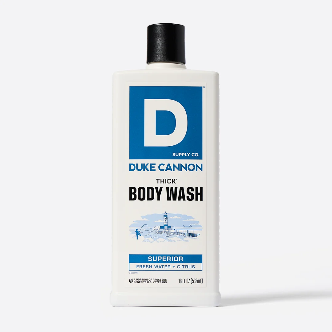 White, rectangular DUKE CANNON SUPERIOR THICK Body Wash bottle with a black cap. Label featuring the logo, product name and a nautical illustration (lighthouse, angler) for the ‘Fresh Water + Citrus’ fragrance. 532ml.
