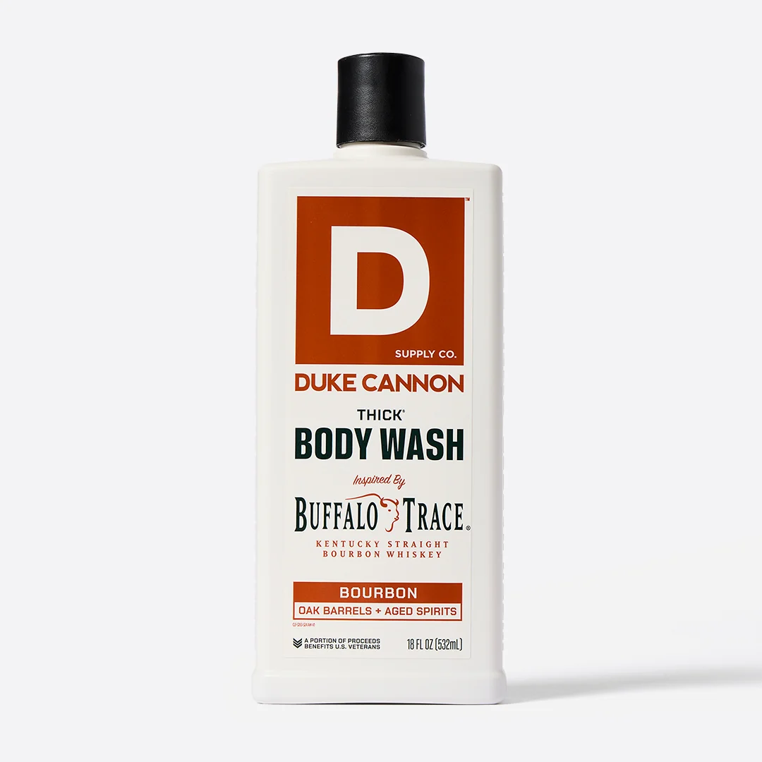Flacon rectangulaire blanc « Duke Cannon Thick Body Wash » avec bouchon à vis noir. Étiquette blanche et rouge-brun ornée d’un grand logo « D ». Texte : « THICK BODY WASH », inspiré du bourbon Buffalo Trace, aux notes de fûts de chêne. 532 ml.