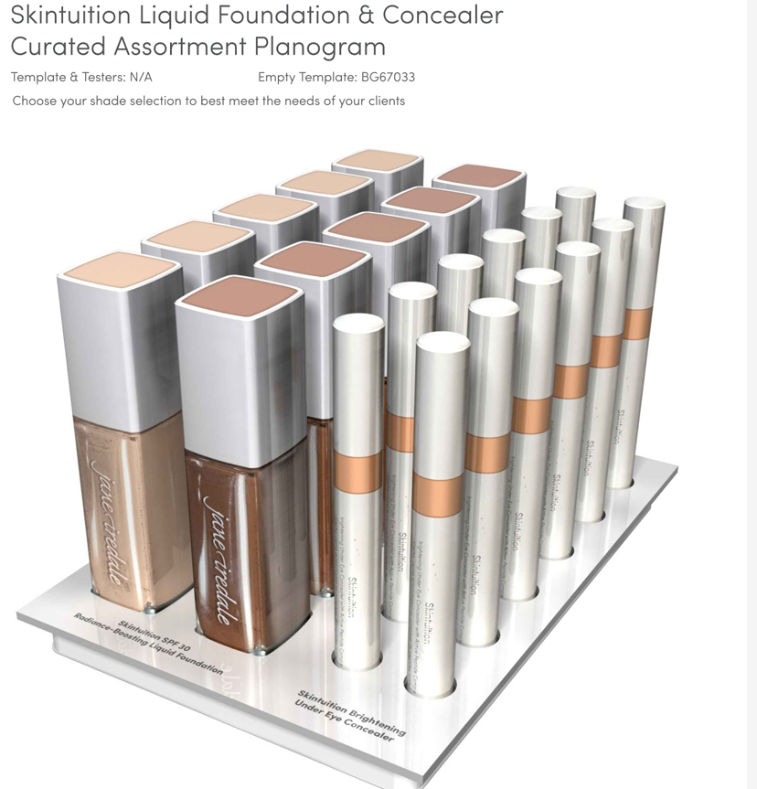 Expositor de Jane Iredale para base Skintuition y corrector de ojeras. En el soporte blanco hay 12 frascos cuadrados de base líquida en distintos tonos de piel y 10 correctores cilíndricos, ordenados.