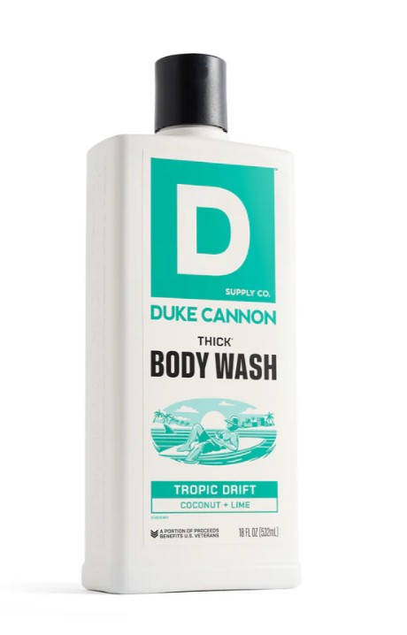 White, rectangular bottle of ‘ DUKE CANNON ’ THICK BODY WASH with a black cap and turquoise label. Label featuring the brand name, “THICK BODY WASH”, a tropical beach illustration (palm tree, surfer) and the “TROPIC DRIFT” coconut & lime fragrance. 532ml.