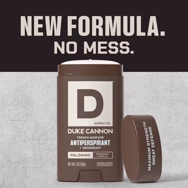 Open brown DUKE CANNON Trench Warfare deodorant stick with white product, cap next to it. Label: Brand, Palomino fragrance (mahogany/vanilla), 85 g. Top: “NEW FORMULA. NO MESS.”, cap: “MAXIMUM STRENGTH SWEAT DEFENCE”.