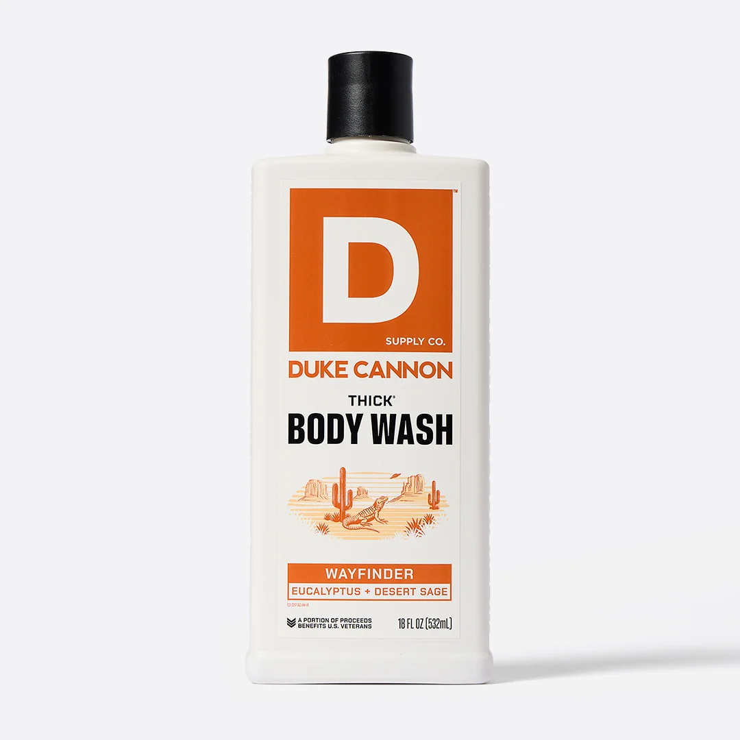 White, rectangular bottle of DUKE CANNON THICK BODY WASH with a black cap. Orange label featuring a large ‘D’ logo and a desert landscape (cacti, lizard skeleton). WAYFINDER fragrance: Eucalyptus & desert sage. 532 ml.