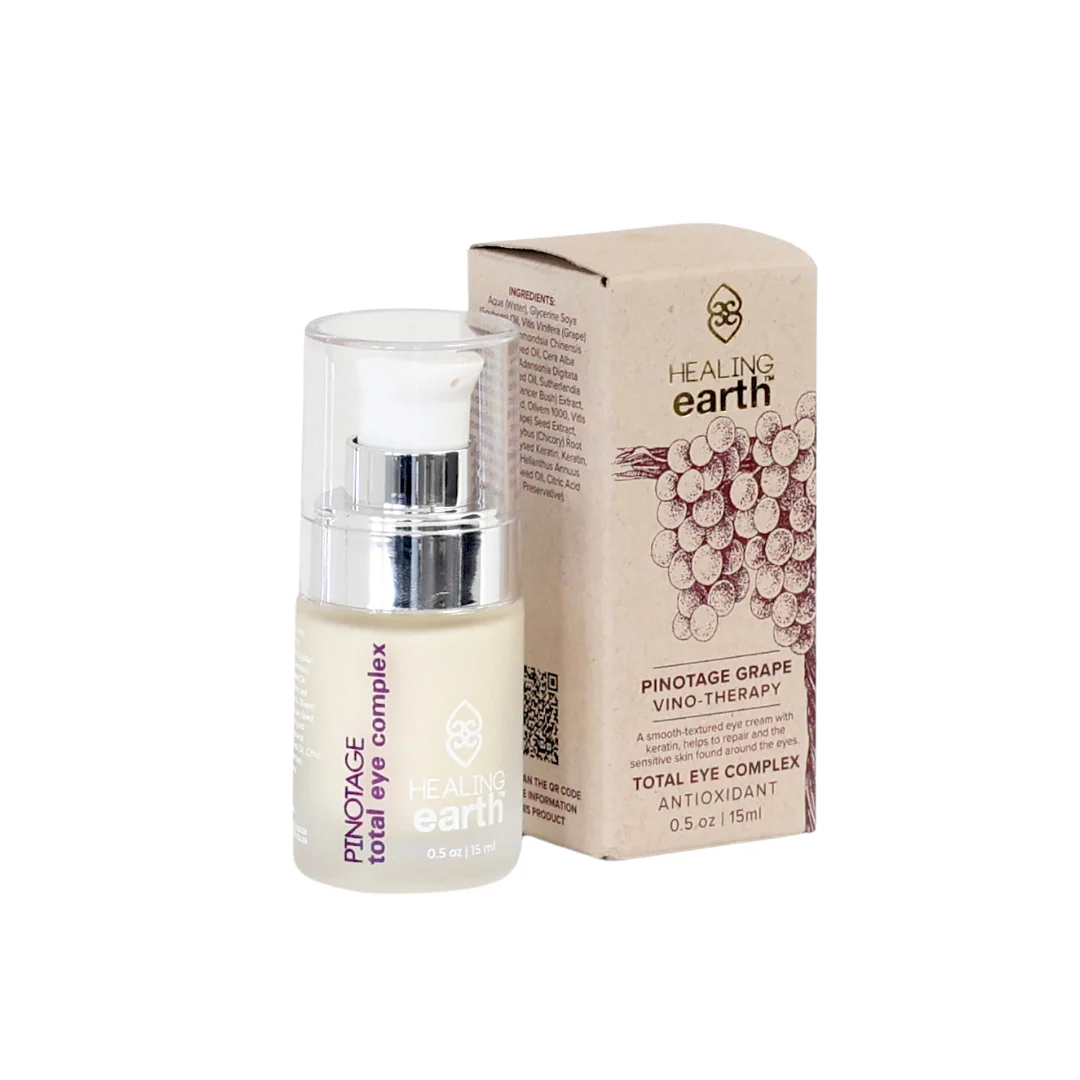 Un flacone beige chiaro di Healing Earth Total Eye Complex con pompa è accanto a una scatola di cartone marrone. Entrambi riportano "Pinotage Total Eye Complex" e il logo Healing Earth; la scatola ha un motivo a grappoli d'uva.