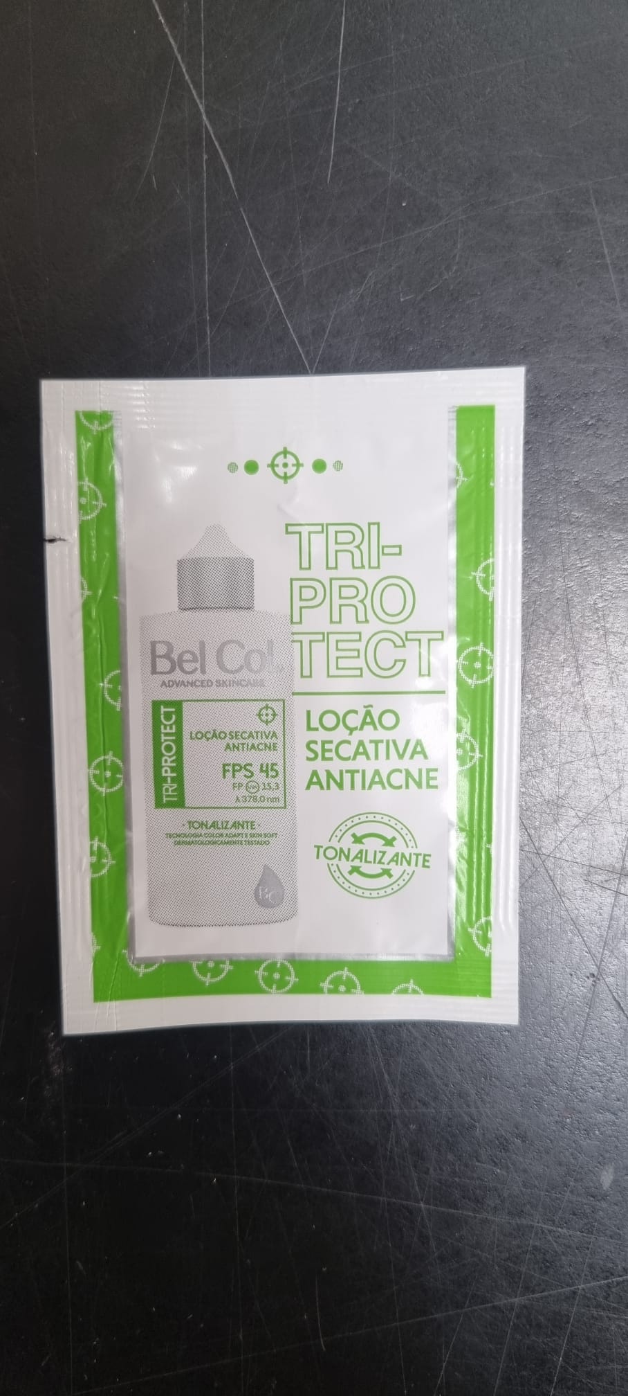 Sachet blanc d'échantillon 1 ml de lotion de jour anti-acné Bel Col Tri-Protect SPF 45. Inscription verte « TRI-PROTECT », « LOÇÃO SECATIVA ANTIACNE », « TONALIZANTE » et flacon. « Bel Col Advanced Skincare » visible.
