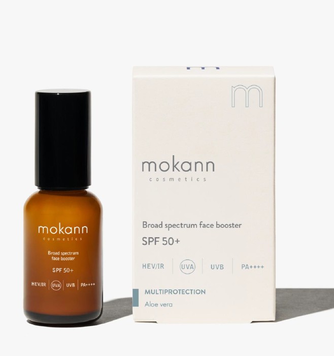 Flacon en verre brun Mokann Cosmetics avec bouchon noir, booster visage SPF 50+ à large spectre, à côté d'un étui carton beige. Protège HEV/IR, UVA, UVB, PA++++, avec aloe vera pour protection multiple.