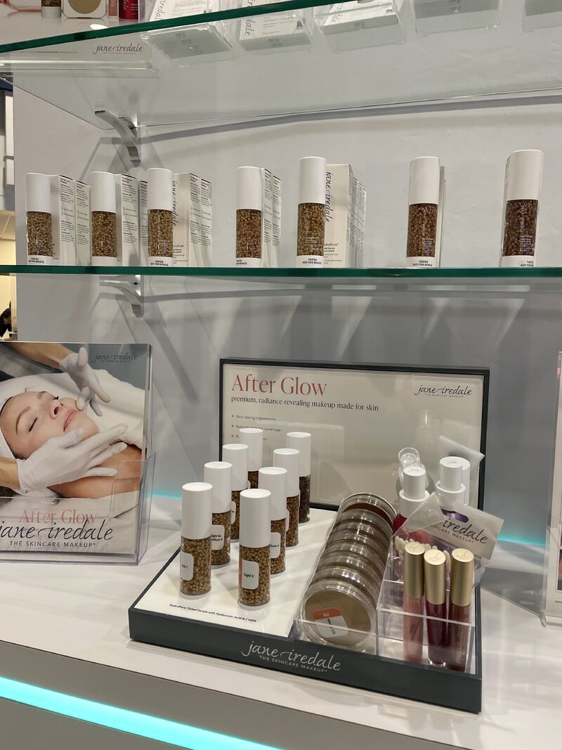 Espositore professionale Jane Iredale: sieri Hydro Pure Color Correction con particelle dorate, Corrective Colors, correttore per il contorno occhi Skintuition e prodotti per le labbra su scaffali, oltre al cartellone pubblicitario “After Glow”.